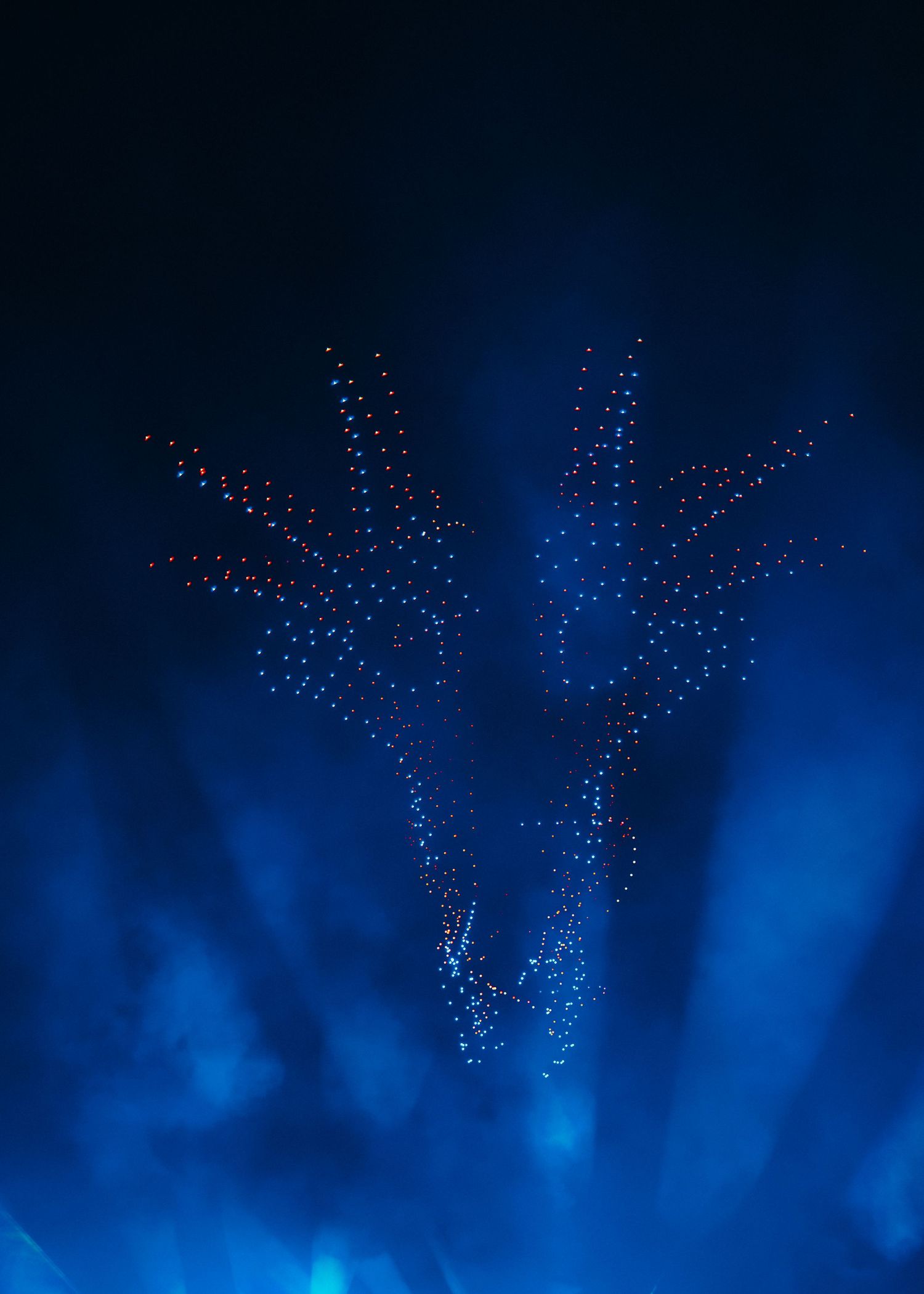 A swarm of illuminated drones forms intricate patterns against a dark blue night sky during a synchronized light show.