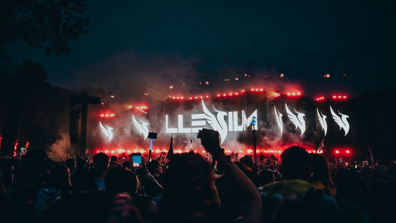 Concert crowd silhouettes against red stage lighting at a nighttime music festival performance.