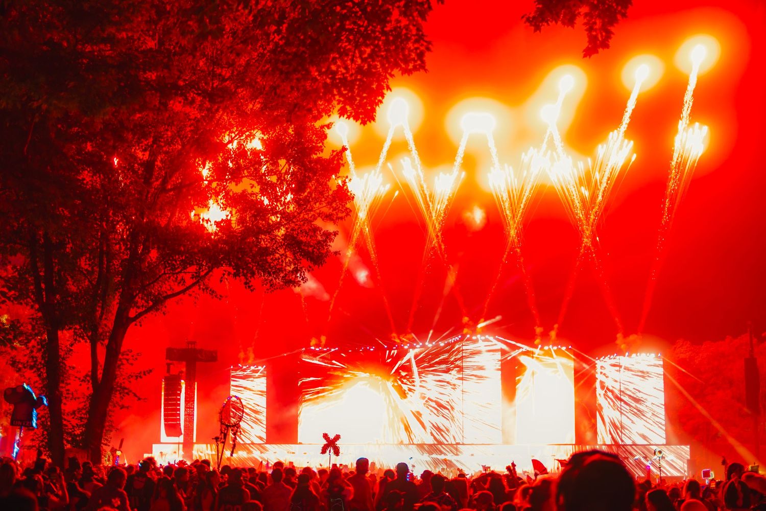 Bright red fireworks illuminate the night sky during an outdoor concert or festival performance.