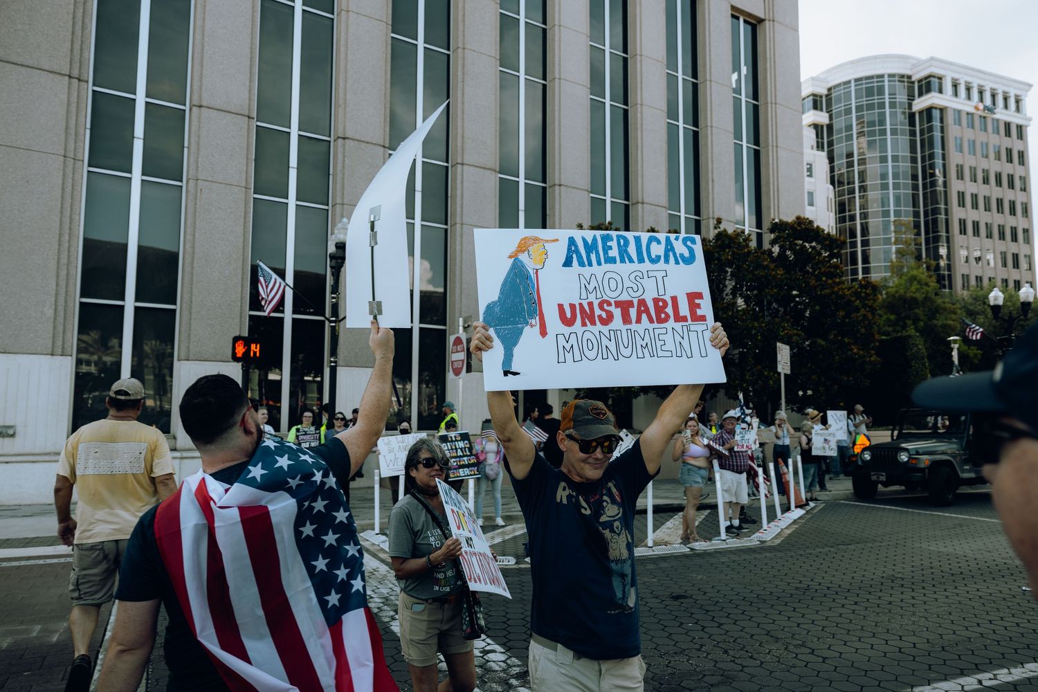 Demonstrators holding protest signs in front of modern office building.