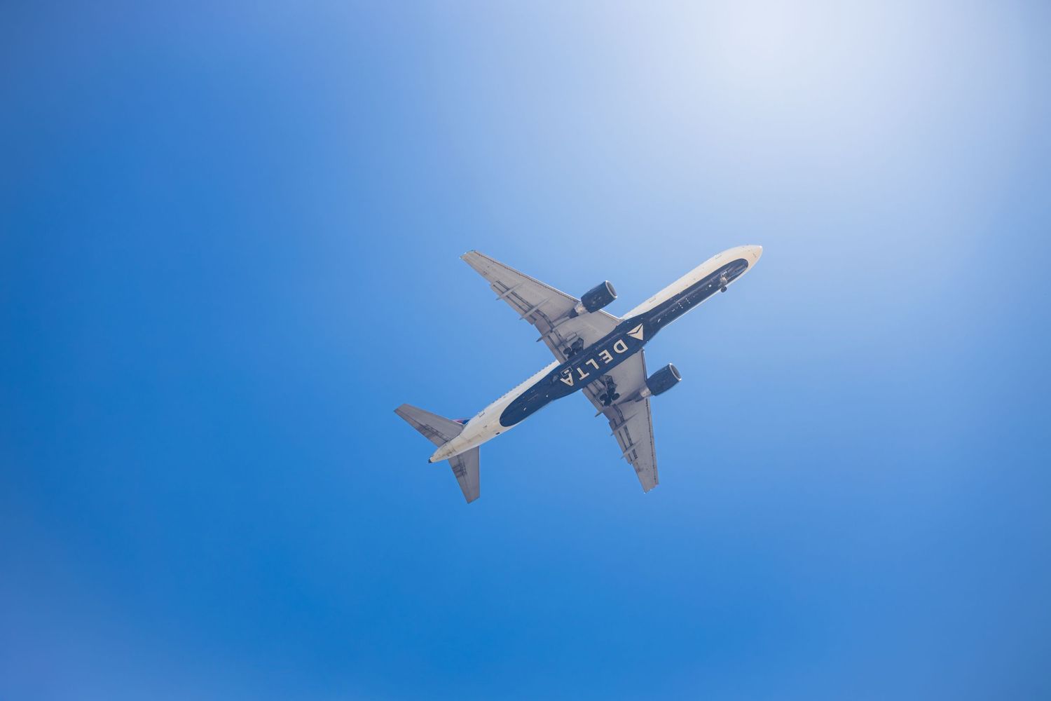 Delta Airlines passenger jet flying overhead against a clear blue sky, viewed from below.