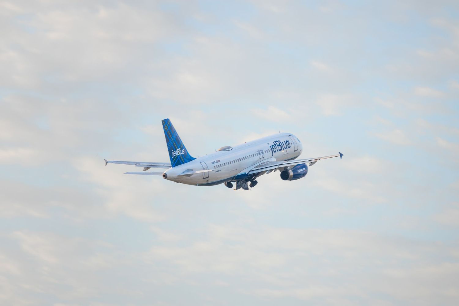 JetBlue Airways Airbus A320 aircraft climbing through partly cloudy skies after takeoff.