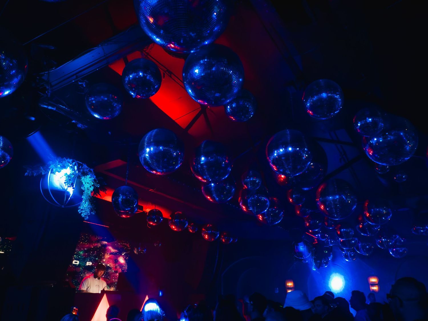 Disco balls reflect blue and red lights across a dark nightclub ceiling creating a vibrant dance atmosphere.
