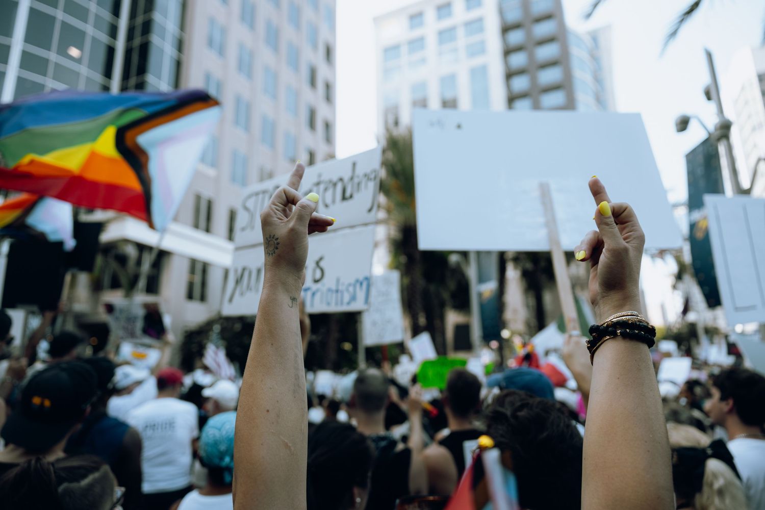 Raised hands holding protest signs among crowd at urban demonstration.