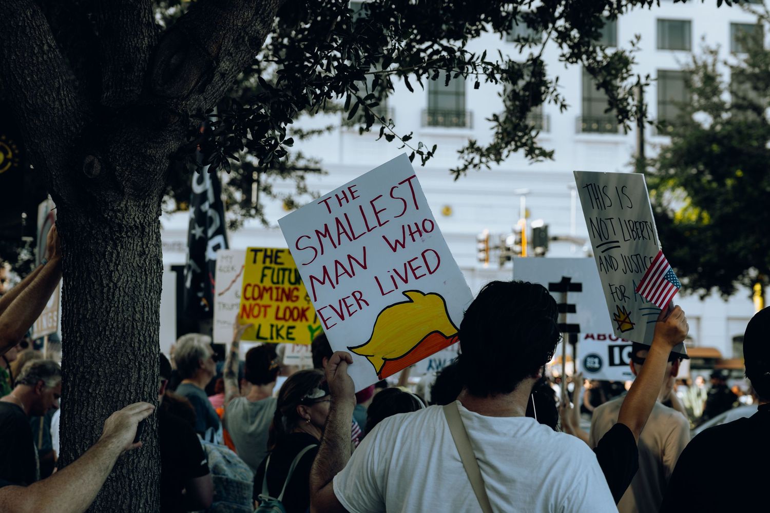 Protesters hold signs during a demonstration with buildings visible in background.