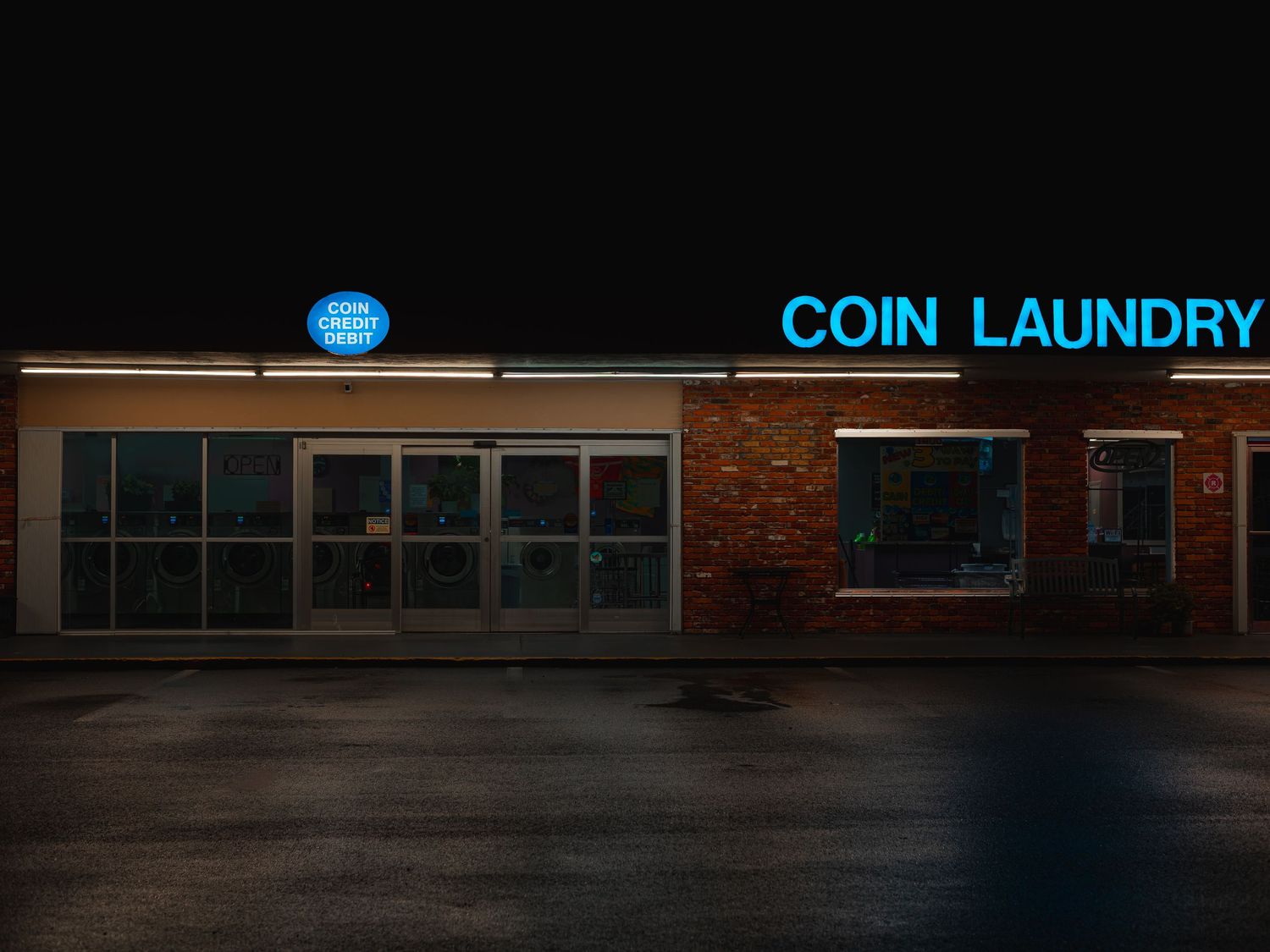 Illuminated neon sign for Coin Laundry glows blue against dark brick building exterior at night.