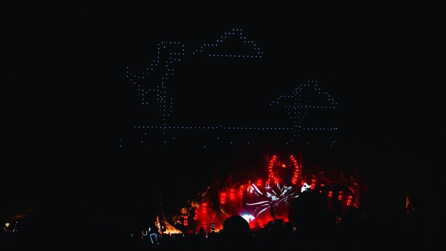 Red illuminated stage lights create a dramatic silhouette against a dark night sky during an outdoor performance.