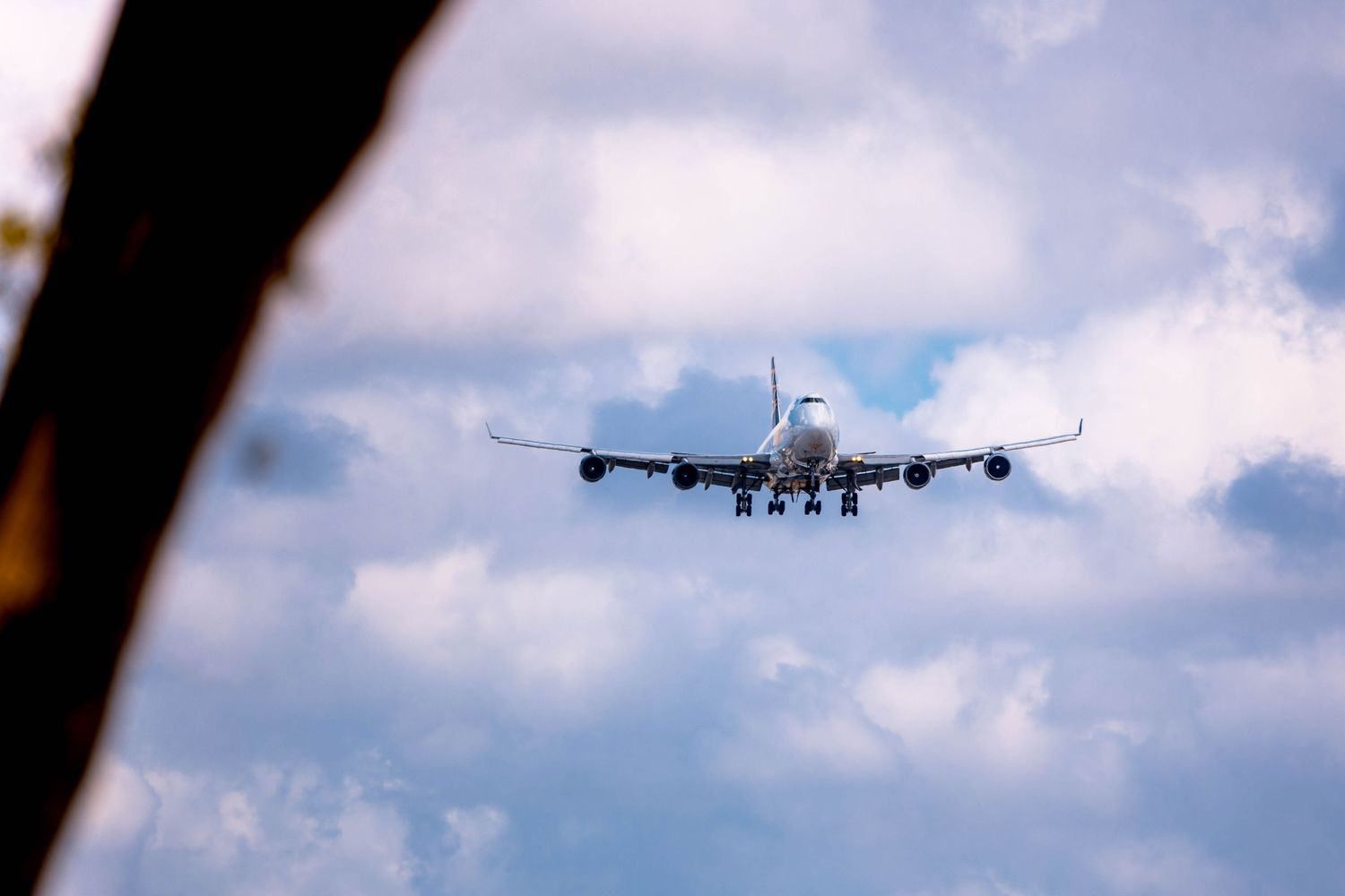 A large commercial Boeing 747 airplane approaching for landing against a cloudy blue sky, viewed from below.