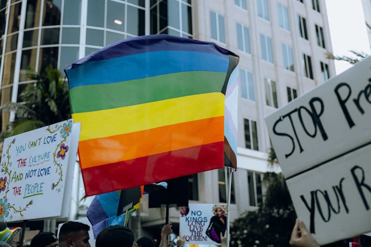 Rainbow pride flag flies against modern office building during protest demonstration.