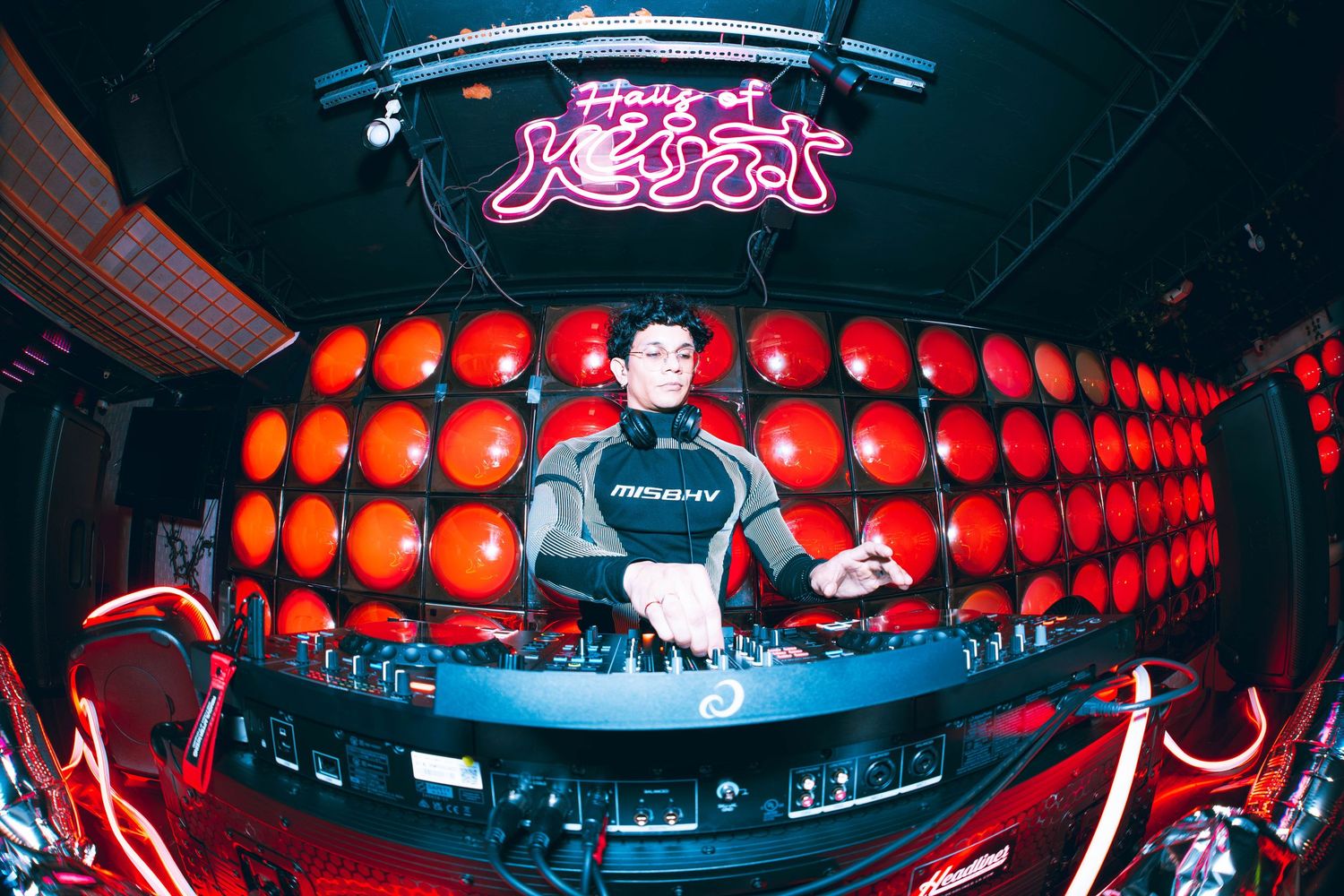 DJ mixing at a club with red sphere wall backdrop and neon signs.