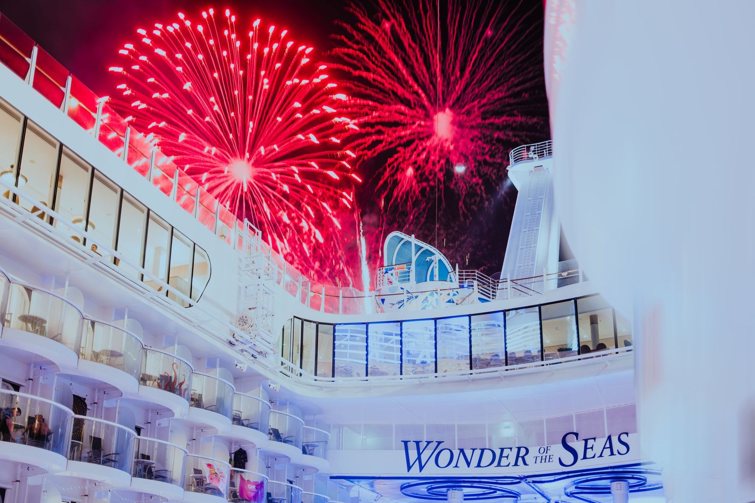 Red fireworks burst over a Royal Caribbean Wonder of the Seas cruise ship at night against a dark sky.