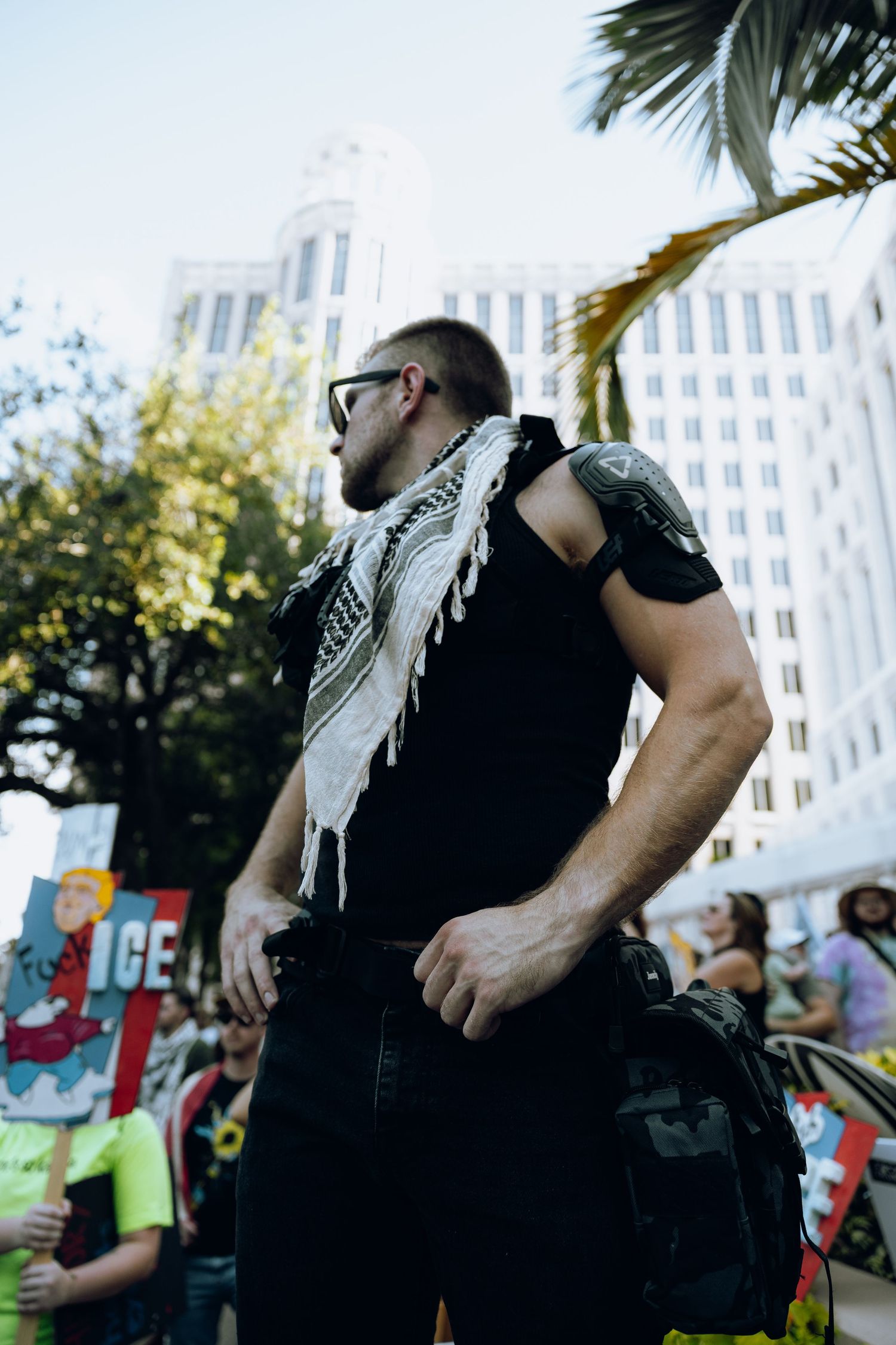 A protester in a black shirt and keffiyeh headscarf gestures animatedly during a street demonstration.