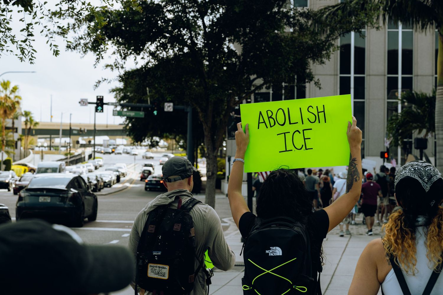Protesters holding a neon green 'Abolish ICE' sign at a demonstration with law enforcement present.