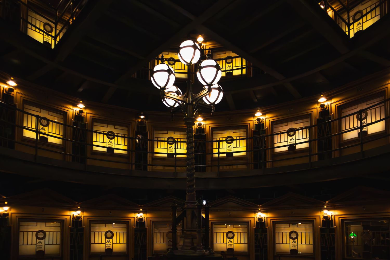 Ornate antique chandelier illuminates a circular room with glowing Art Deco windows in a historic building interior.
