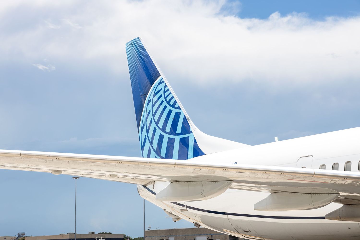 United Airlines airplane tail fin displaying globe logo against a partly cloudy blue sky on airport tarmac.