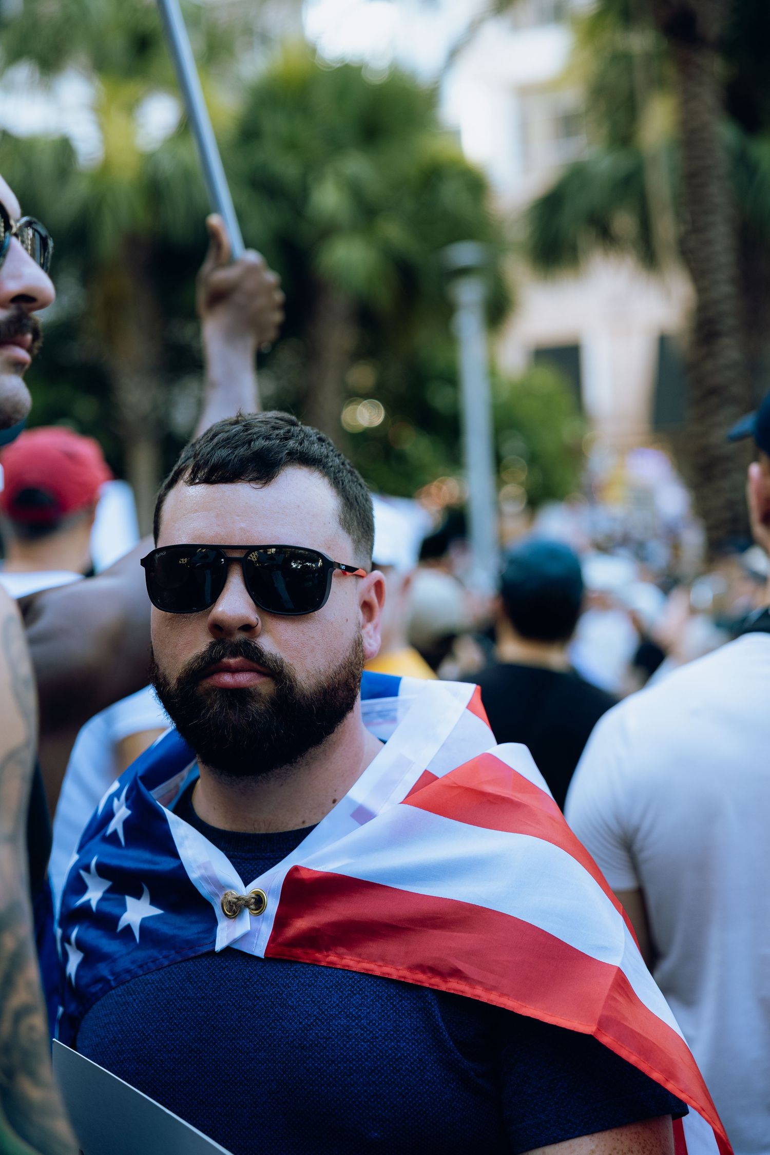 A crowd gathers at a protest with someone wearing an American flag.