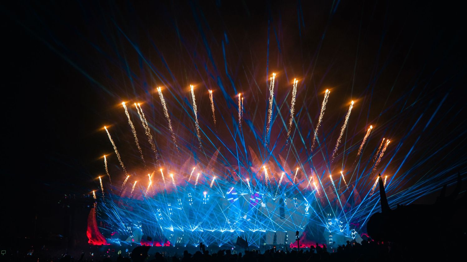 Spectacular fireworks display illuminates the night sky with blue lights and golden sparklers during an outdoor event.