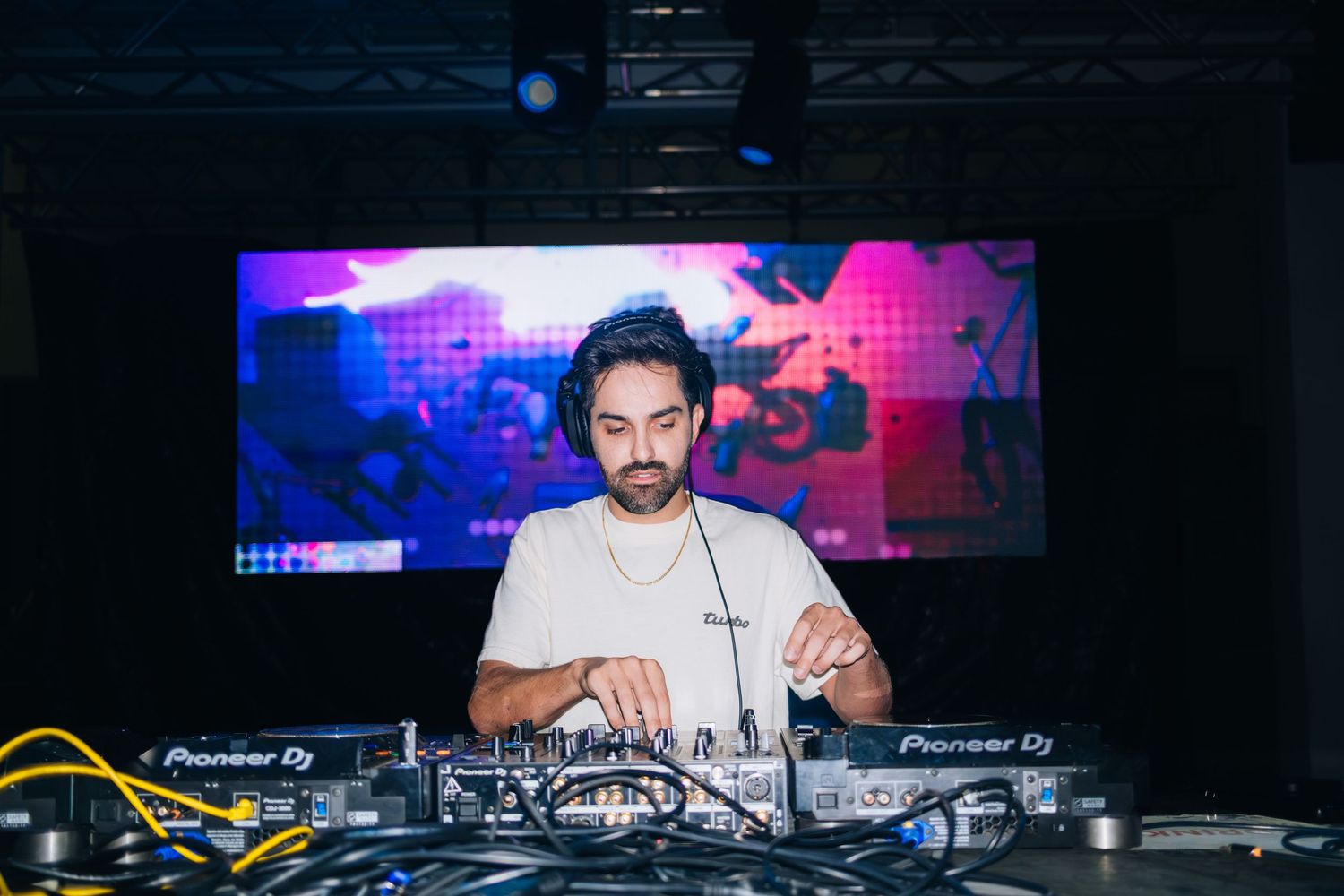 DJ performs behind turntables at a nightclub with colorful lighting and professional equipment in the background.