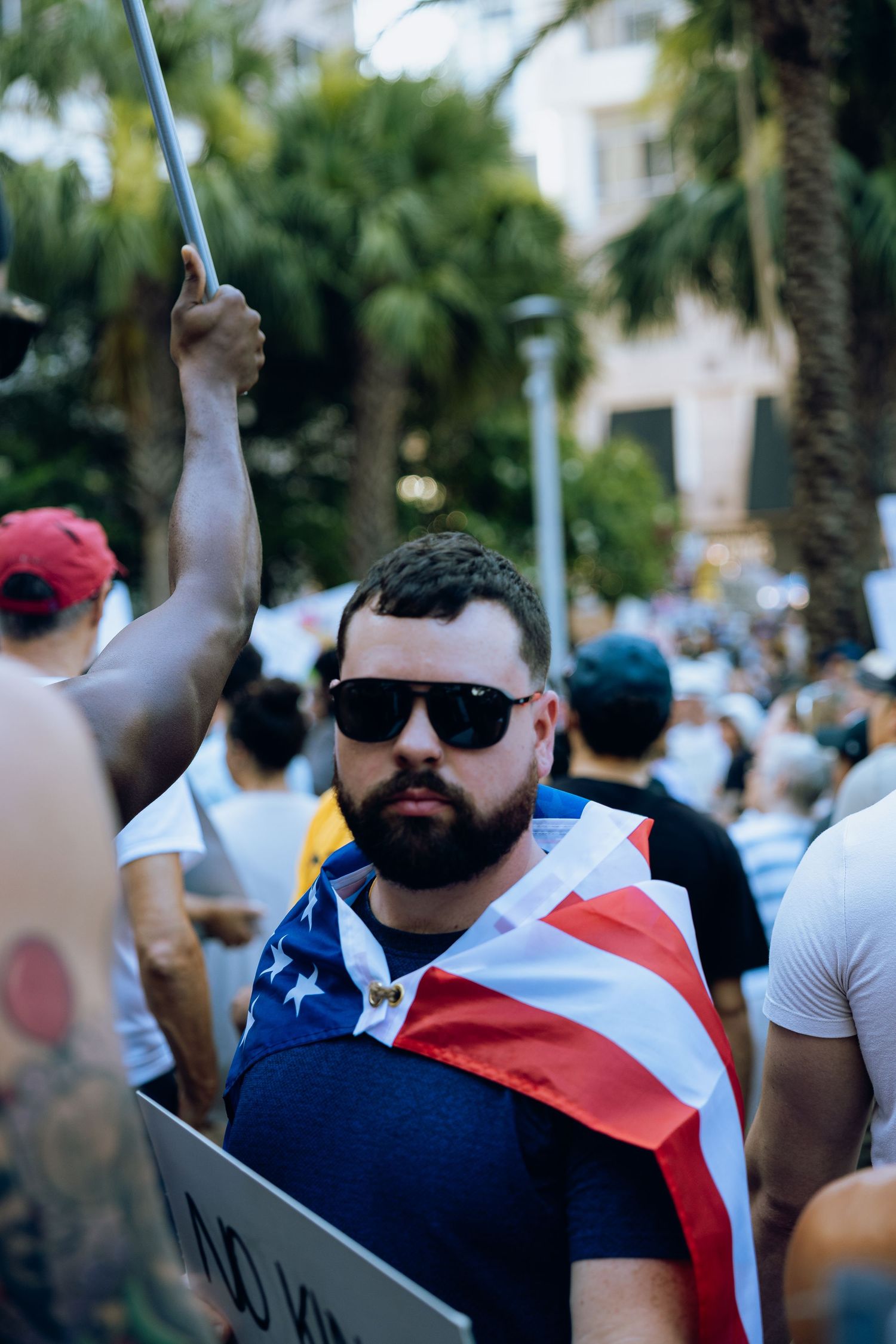 Protestor wearing sunglasses and American flag attire at crowded demonstration.