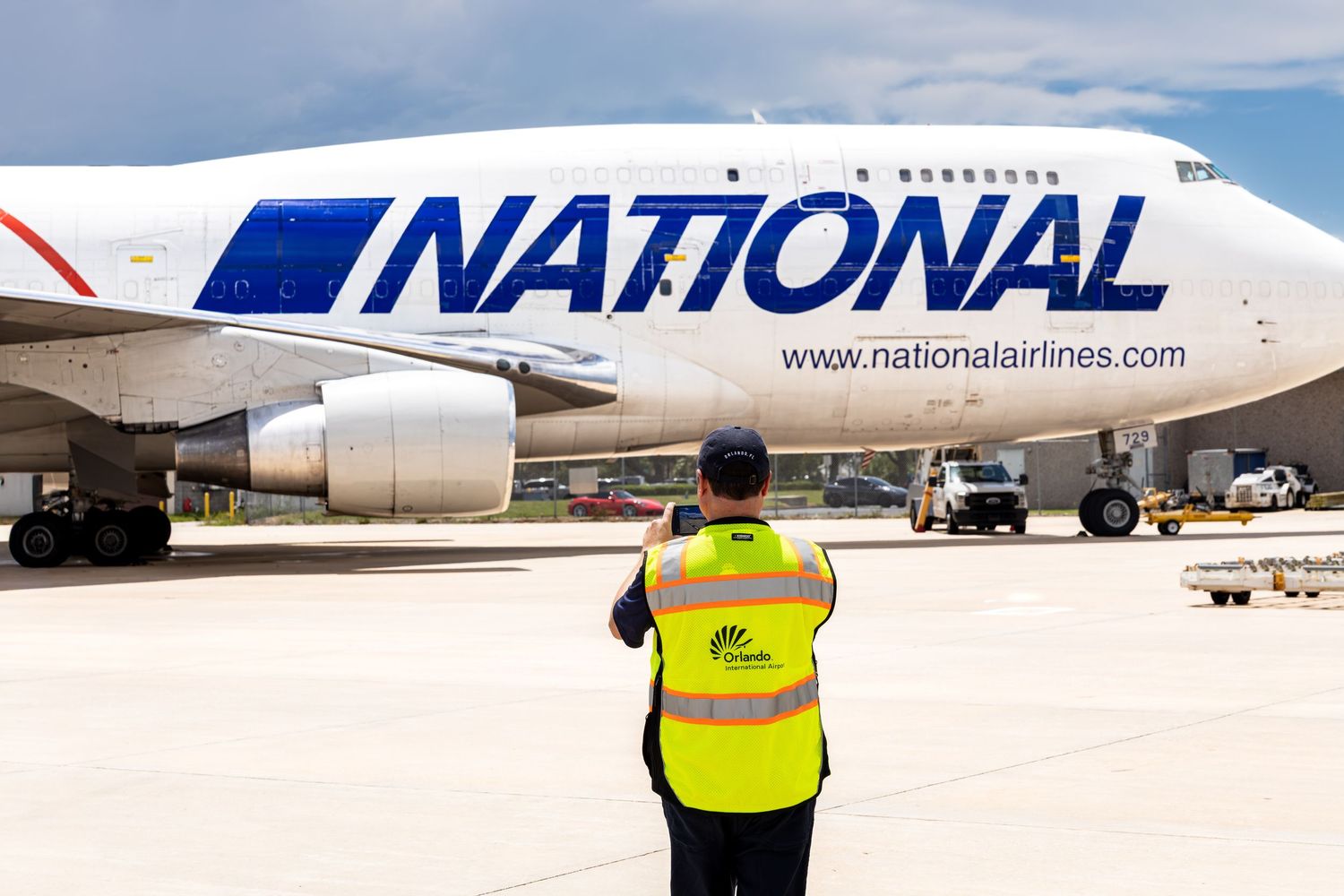 Ground crew member in yellow vest signals a National Airlines Boeing 747 cargo plane on sunny airport tarmac.