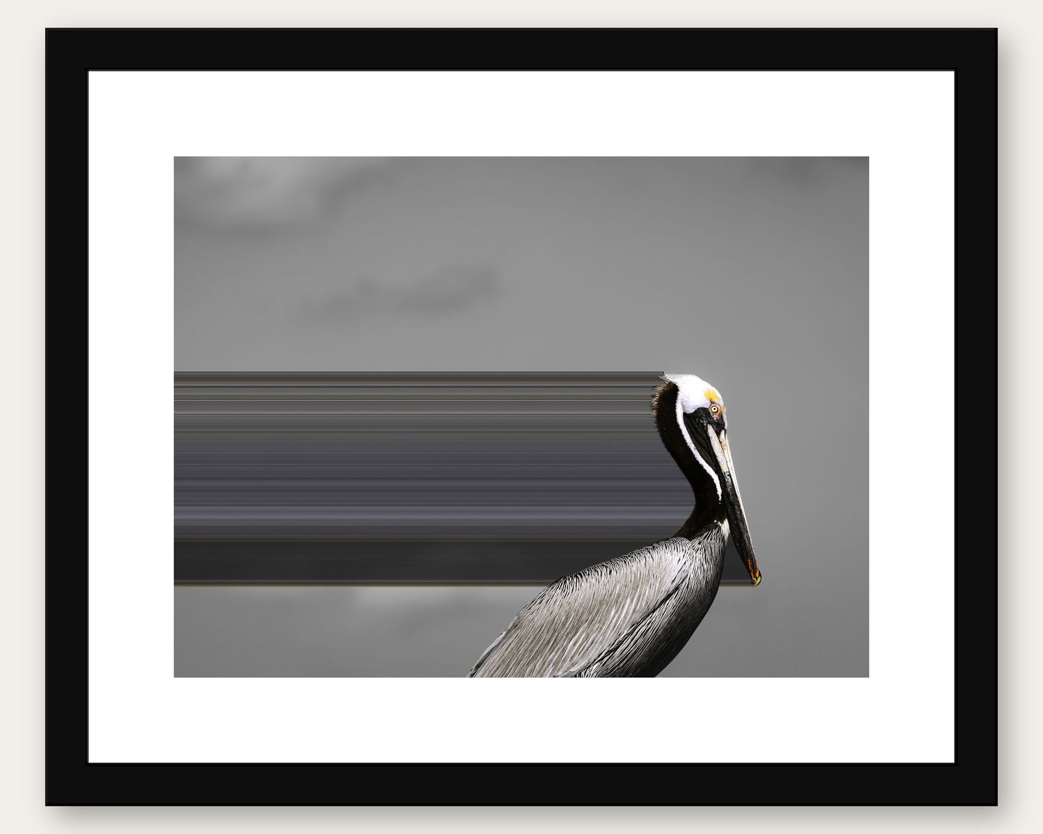 Framed black and white photo of a pelican perched on a railing against a gray cloudy sky.