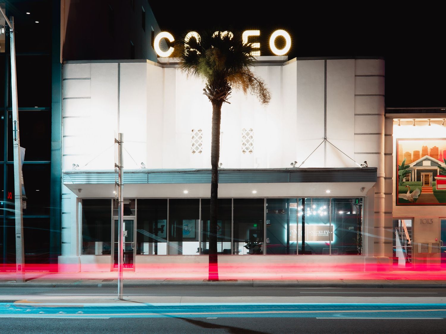 Modern retail storefront with illuminated signage at night with a sleek glass facade and teal-colored lighting.