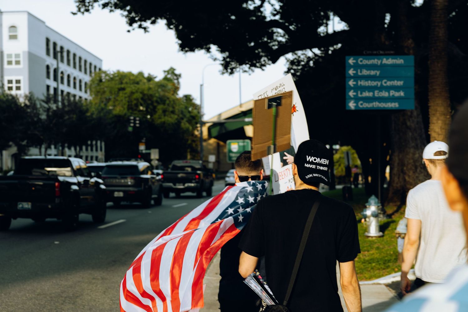 American flag bearer walking down urban street during protest march.