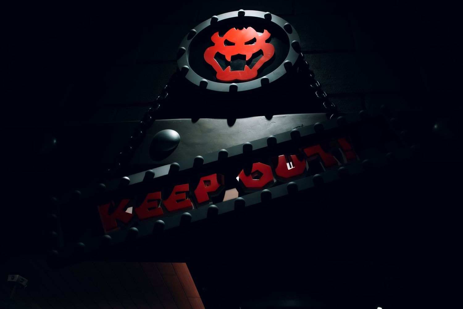 Dark illuminated sign with a neon red bat logo glowing against a black industrial background.