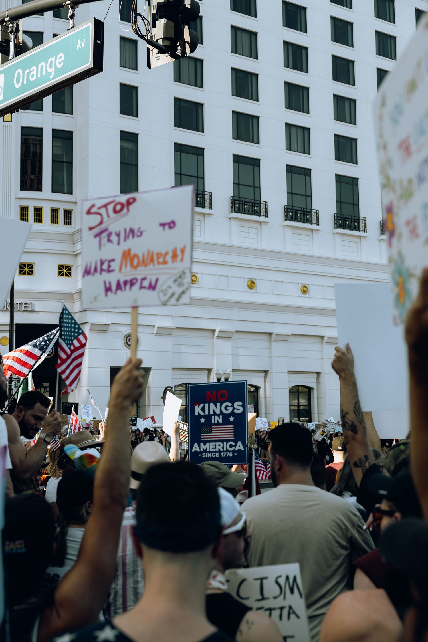 Crowd of protesters holding signs outside a building with an Orange street sign visible.