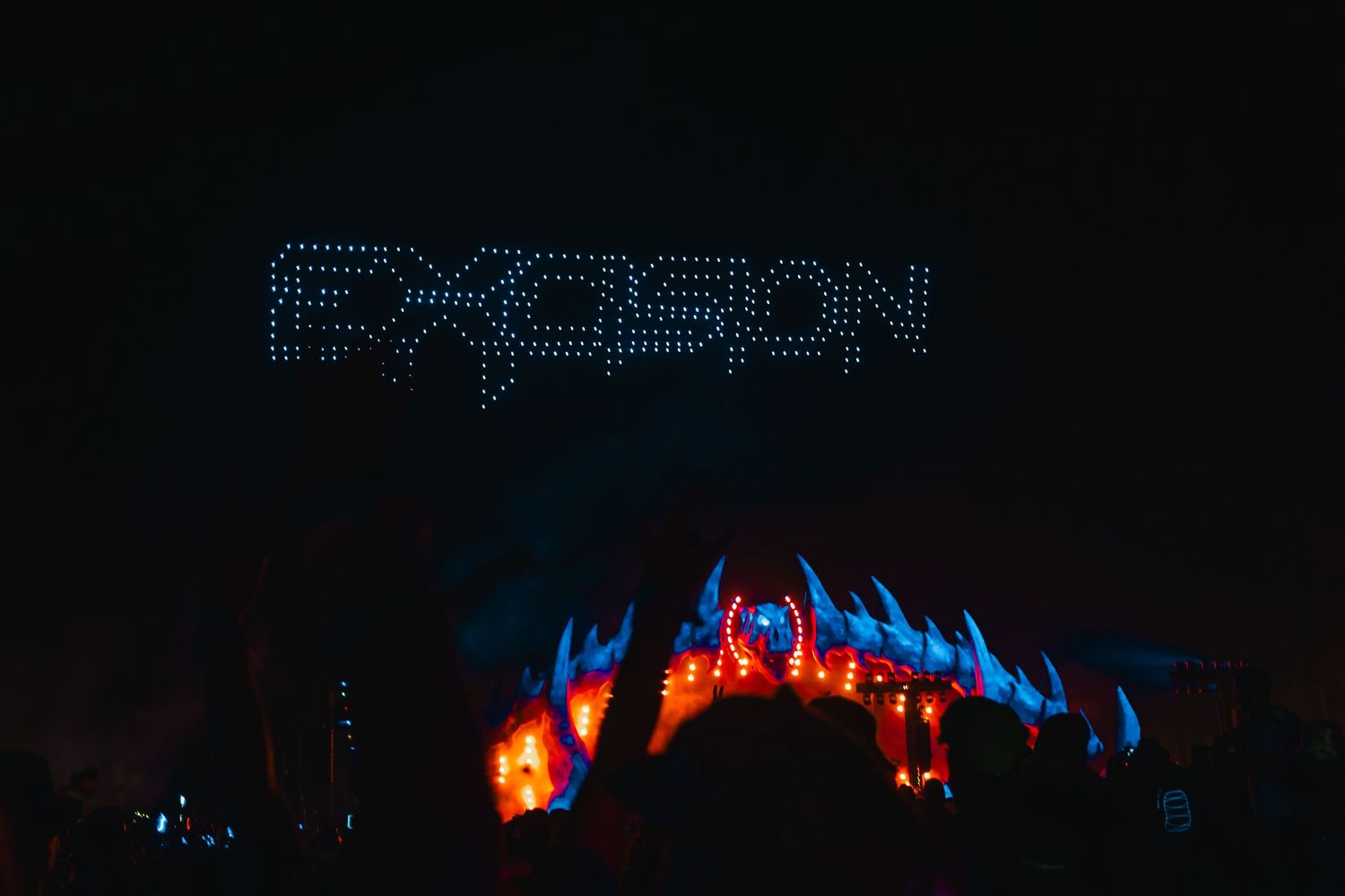 A dark concert stage illuminated with blue and orange lights creates a dramatic performance atmosphere.