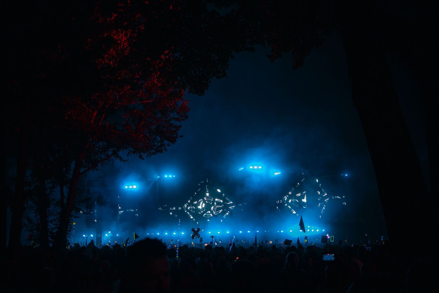 Blue stage lights illuminate a dark concert venue with silhouettes of performers and equipment visible against the glow.