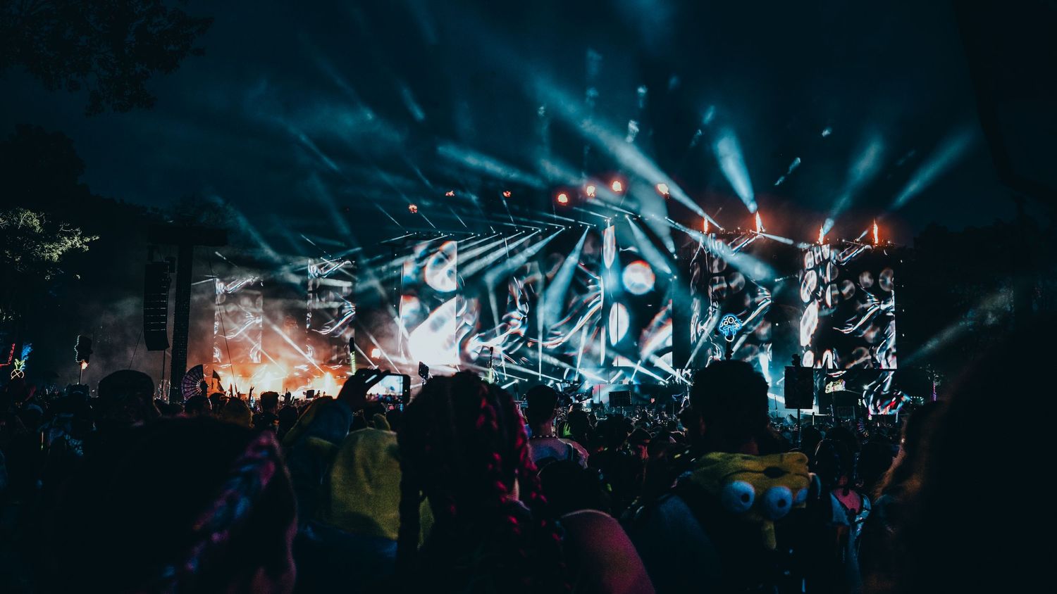 Panoramic view of a crowded concert venue with colorful stage lighting and silhouettes of audience members.
