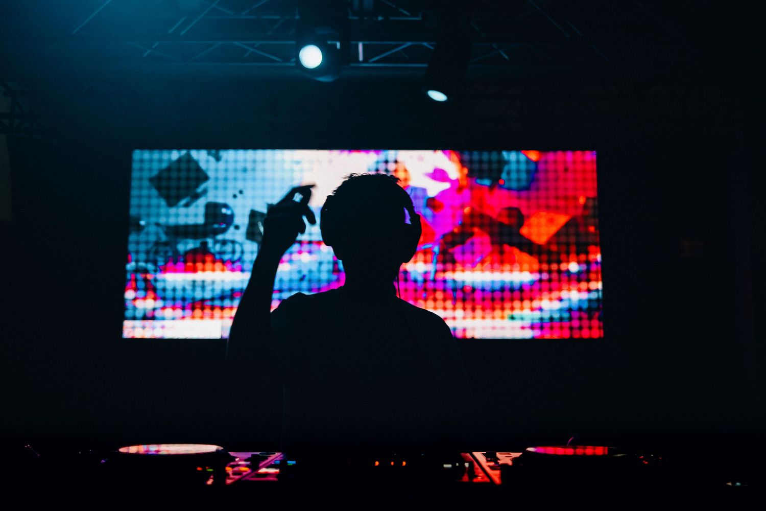 A silhouetted DJ performs on stage against a vibrant digital display screen showing colorful patterns and lights.