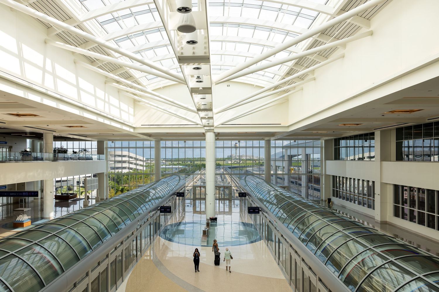 Modern airport terminal atrium with glass ceiling, escalators, and natural light flooding the spacious interior.