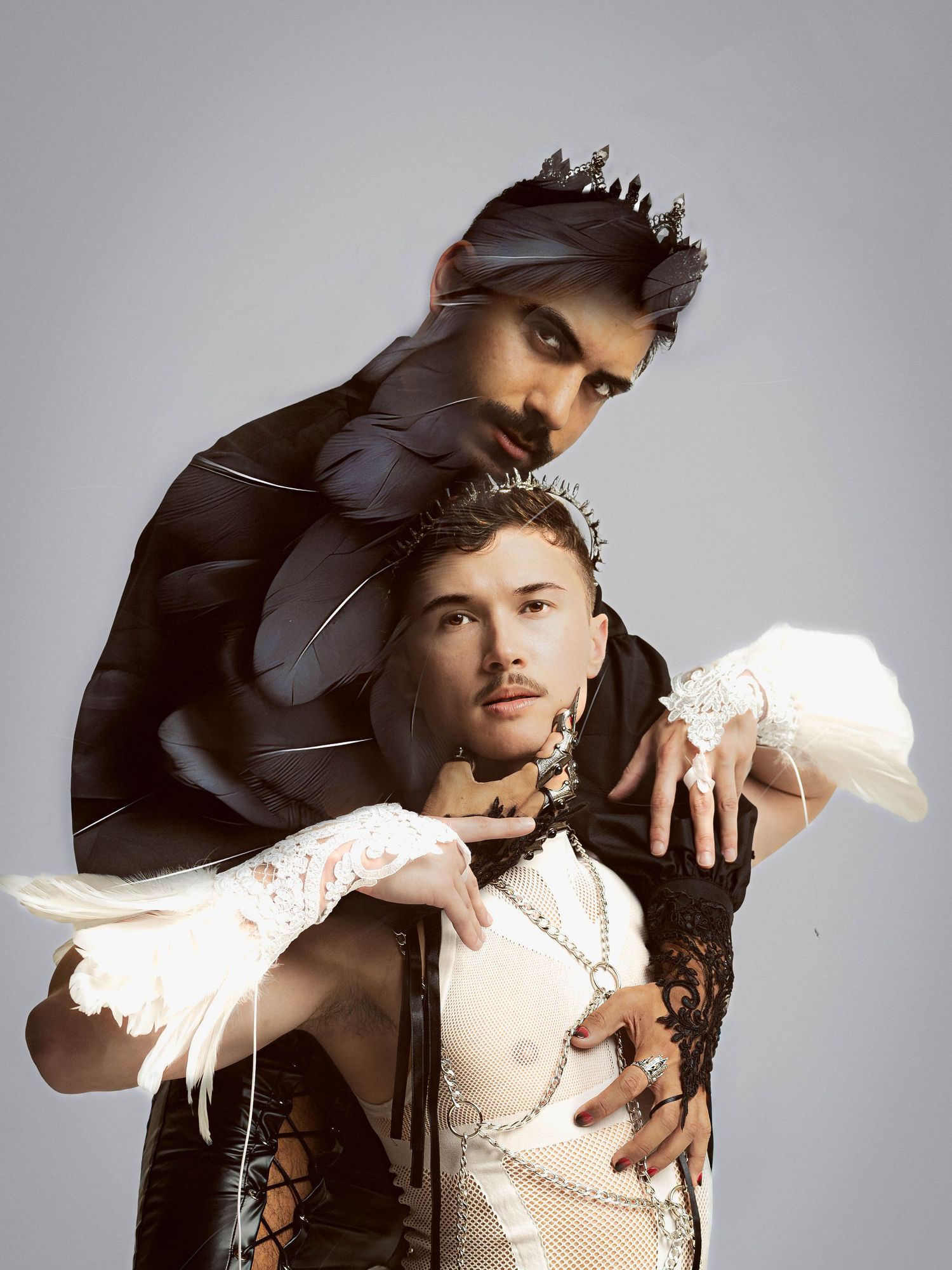 Two performers in dramatic black and white avant-garde costumes pose together against a gray studio background.