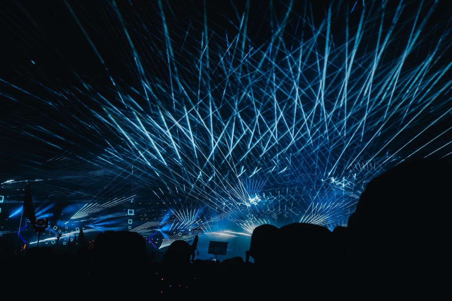 Blue laser beams create a geometric light show pattern against a dark background during a concert performance.