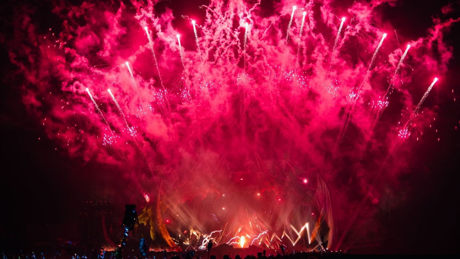 Vibrant pink and red fireworks bursting across the night sky in a dramatic panoramic display.