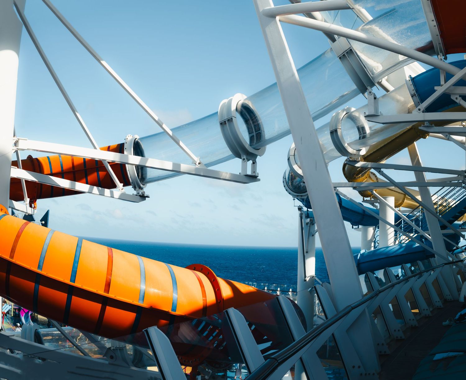 Orange and white lifeboats mounted on the side of a cruise ship against a bright blue sky.