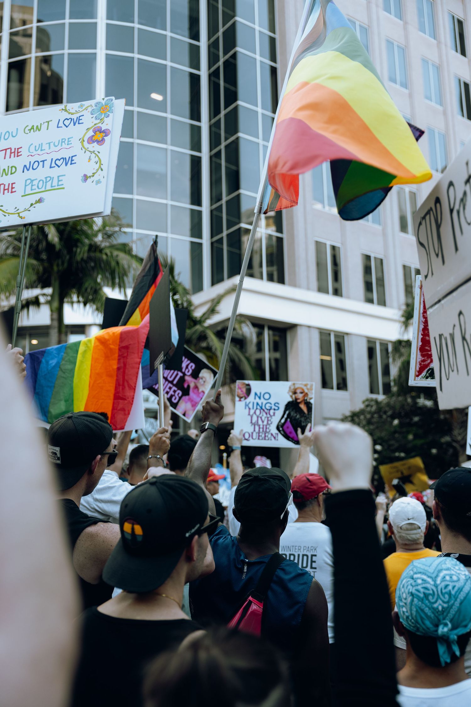 Rainbow flags and protest signs held high during demonstration near office building.