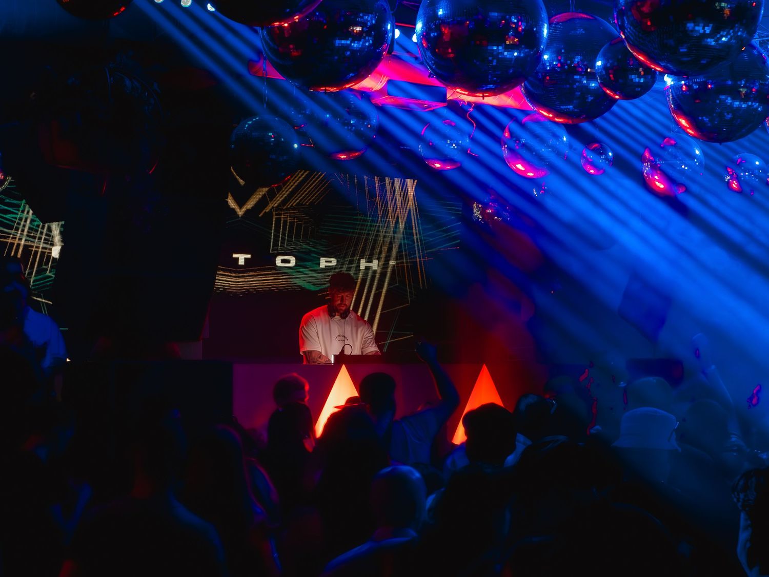 Blue laser beams illuminate a dark nightclub with red lighting effects creating an atmospheric dance party environment.