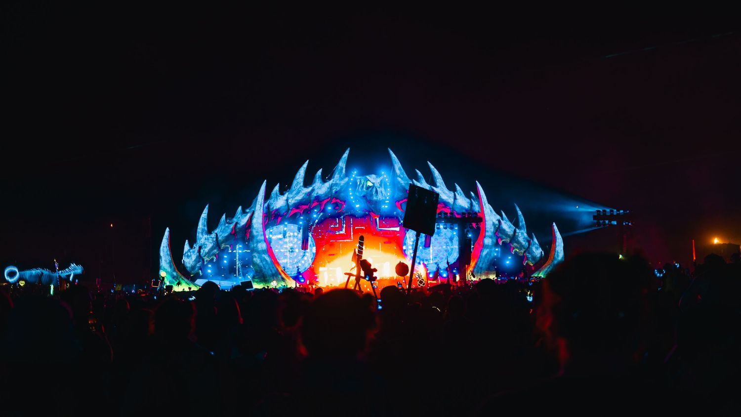 Colorful illuminated art installations glowing in blue and red create a dramatic nighttime display at an outdoor festival.