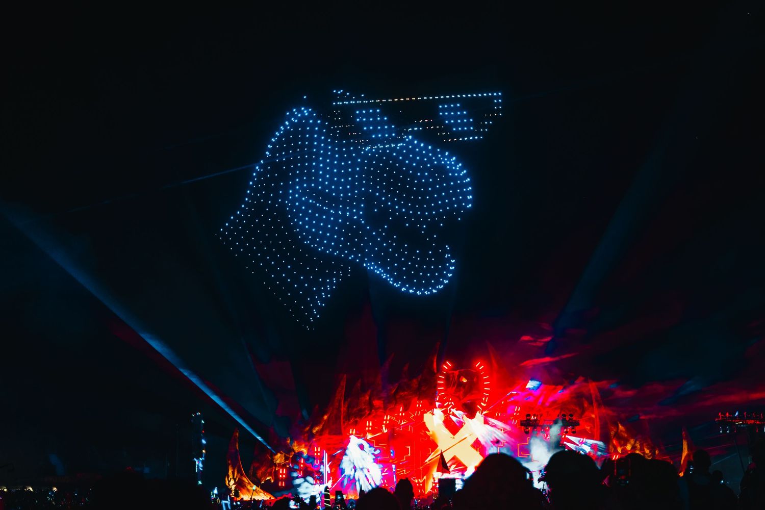 A dramatic concert stage lit with blue and red lights shows illuminated dots forming geometric patterns against a dark background.
