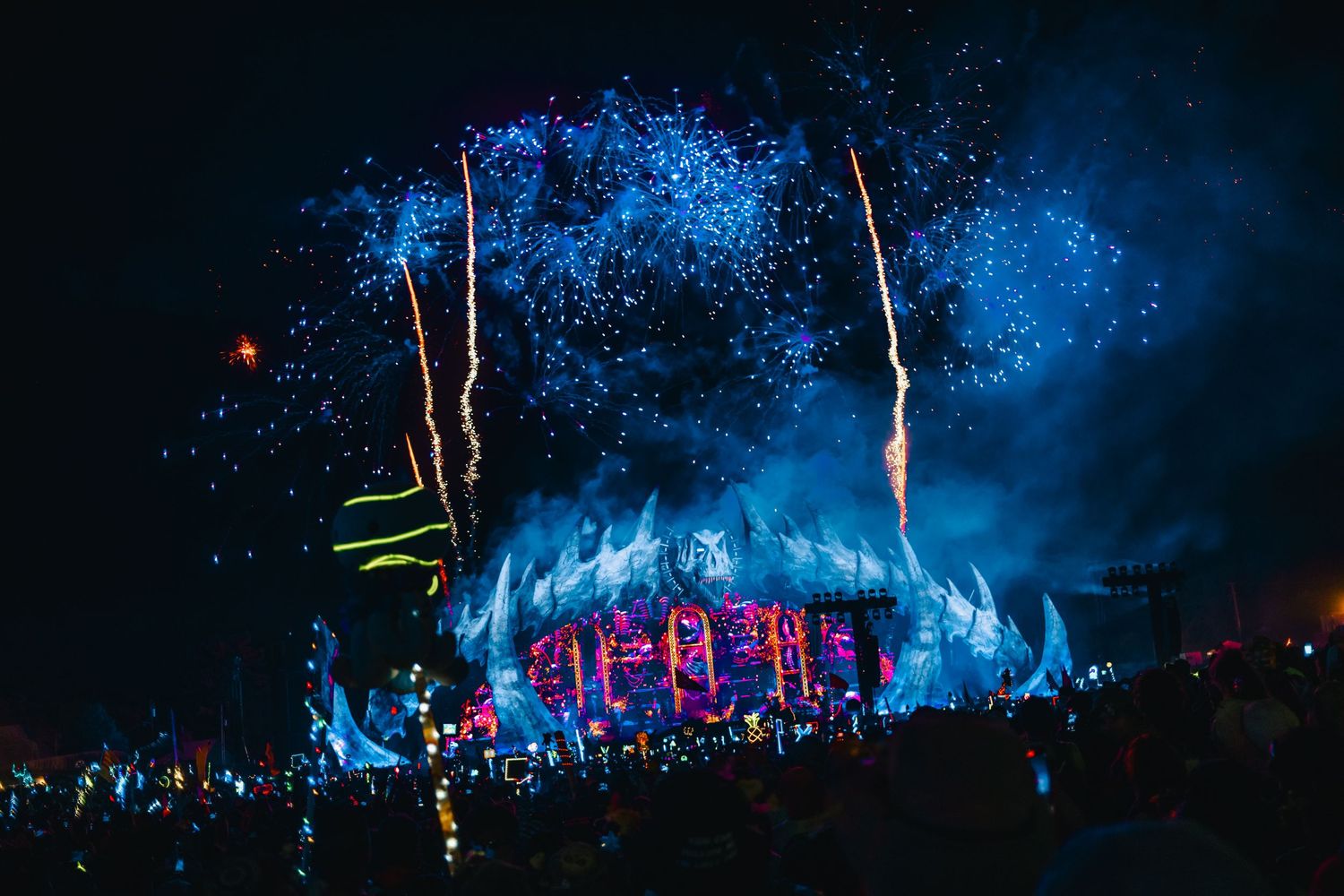 Concert crowd illuminated by blue stage lights and smoke effects during a nighttime outdoor music festival performance.