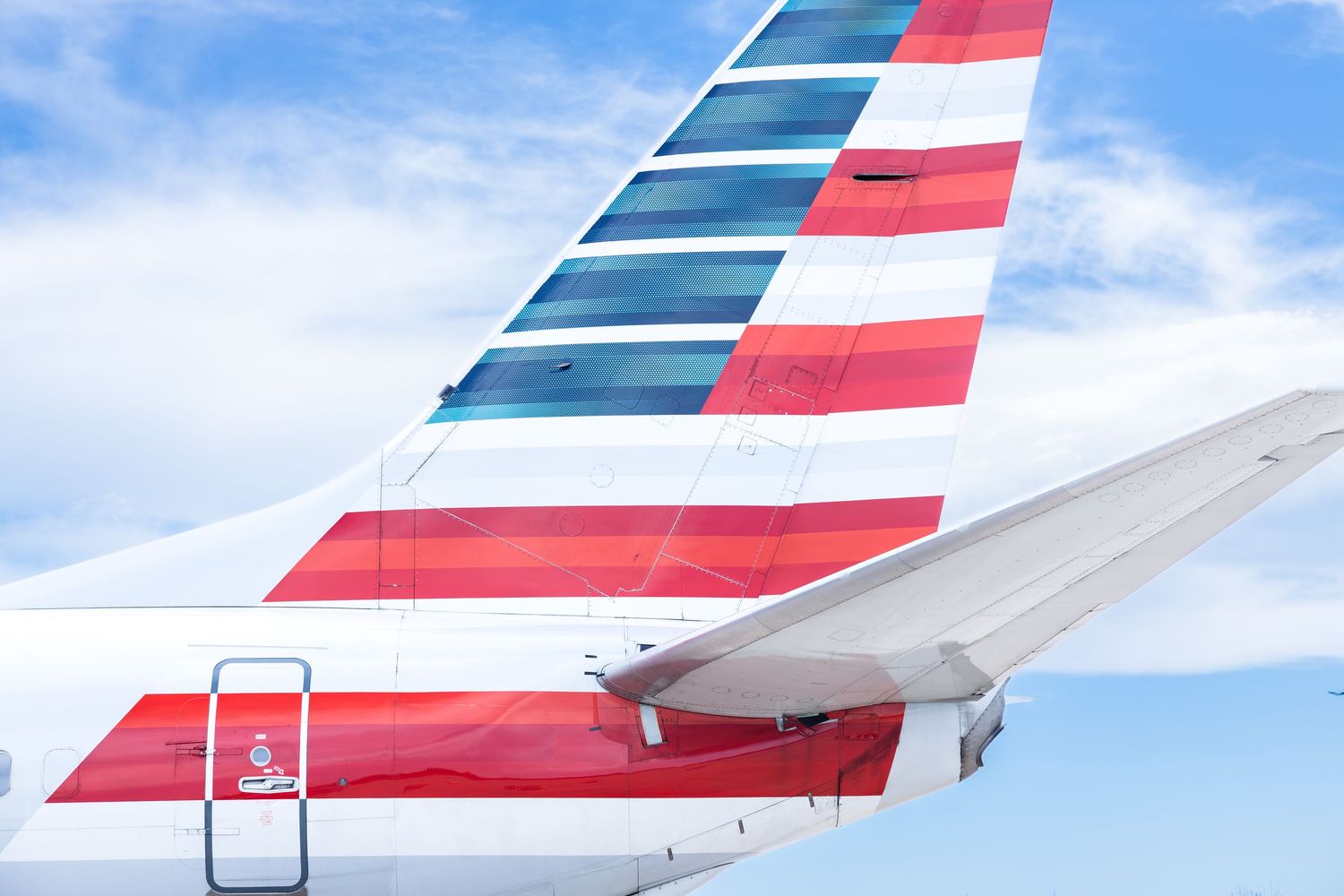 American Airlines plane tail and wing featuring iconic red, white, and blue livery against a blue sky.