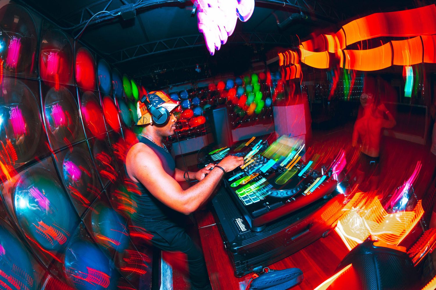 DJ mixing at turntables surrounded by colorful motion-blur lights in an energetic nightclub.