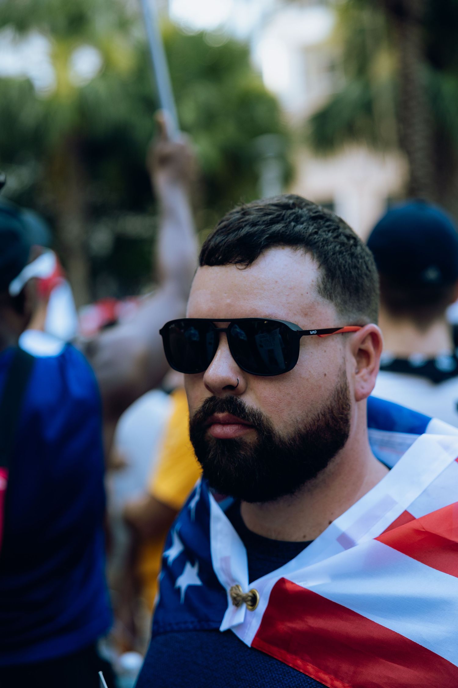 Close-up portrait of demonstrator wearing sunglasses and American flag garment at protest.