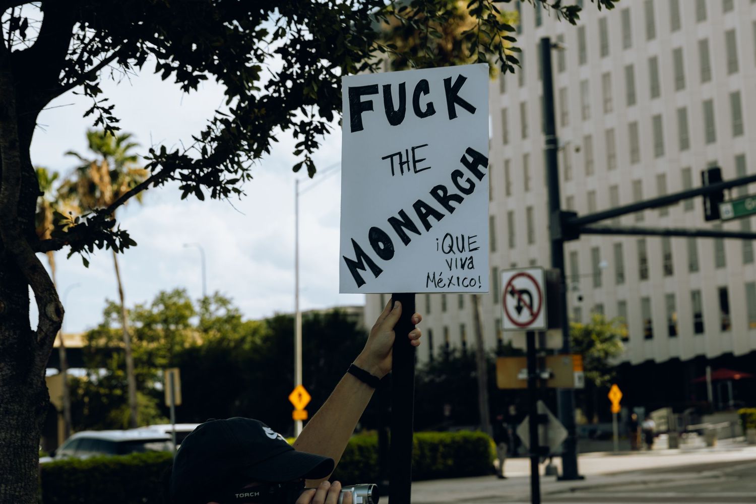Street sign with protest message reading 'Fuck the monarchy' against blurred urban backdrop.