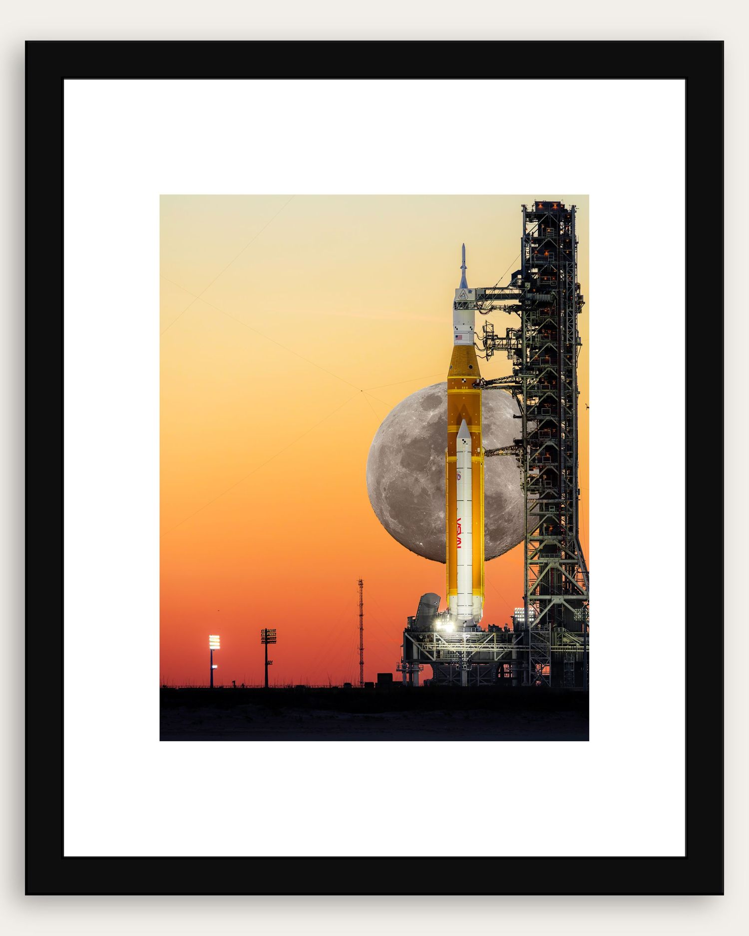 NASA SLS rocket on launch pad at sunset with full moon rising behind it, framed print with black border.