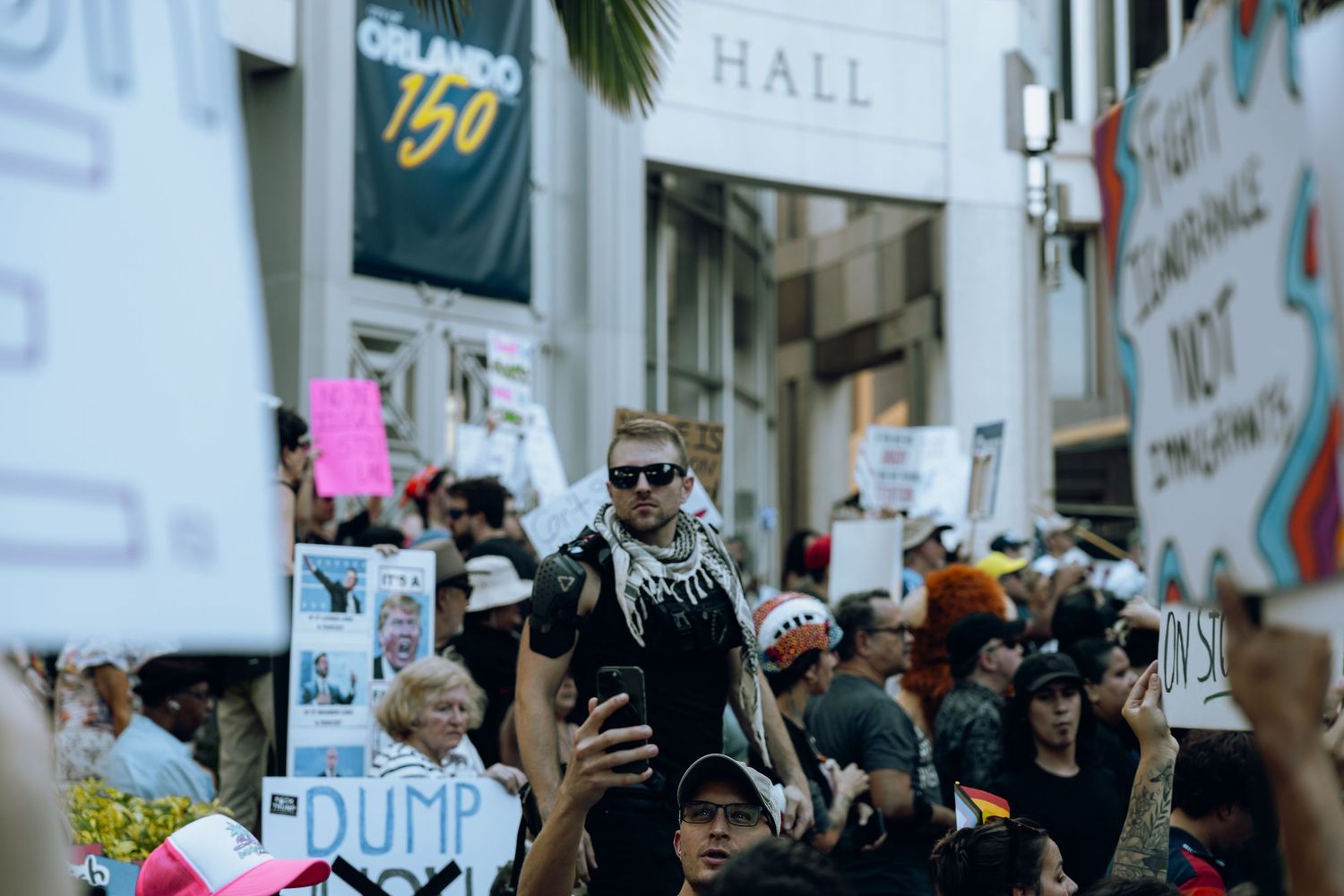 Protesters gather in a crowded city street holding signs and raising their fists during a demonstration.