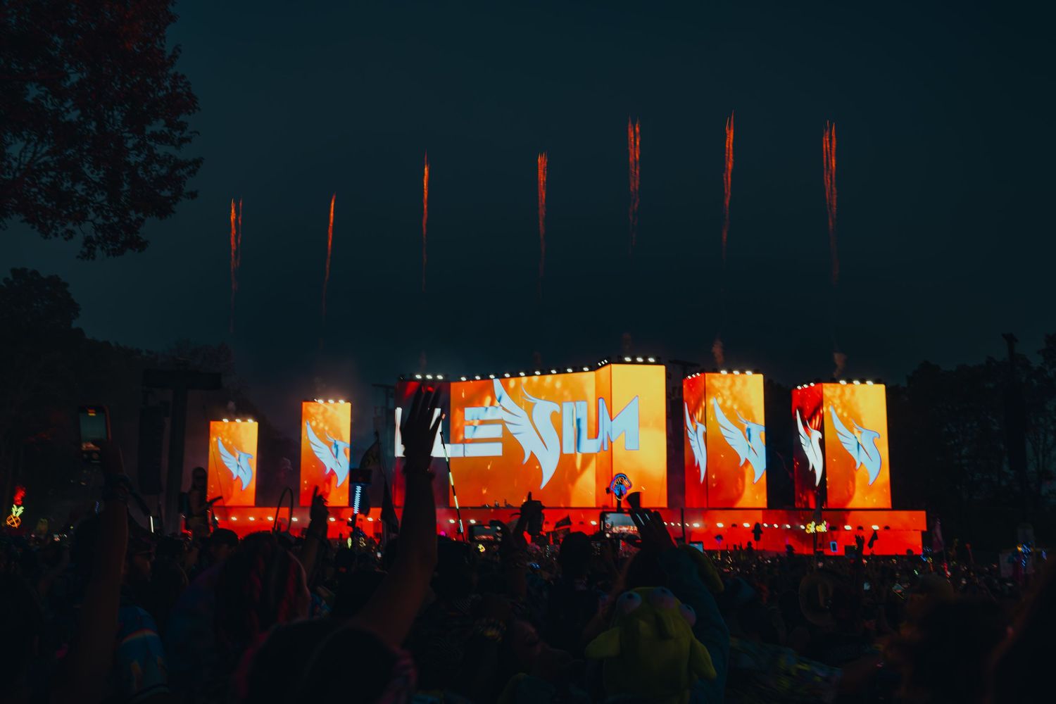 Colorful LED stage screens light up a night music festival crowd with orange graphics and pyrotechnics.